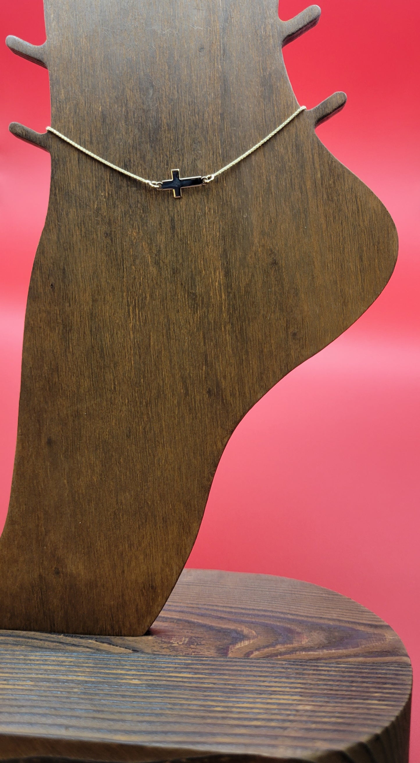 14k yellow gold Cross Anklet on a wooden foot display while on a red color background close up.