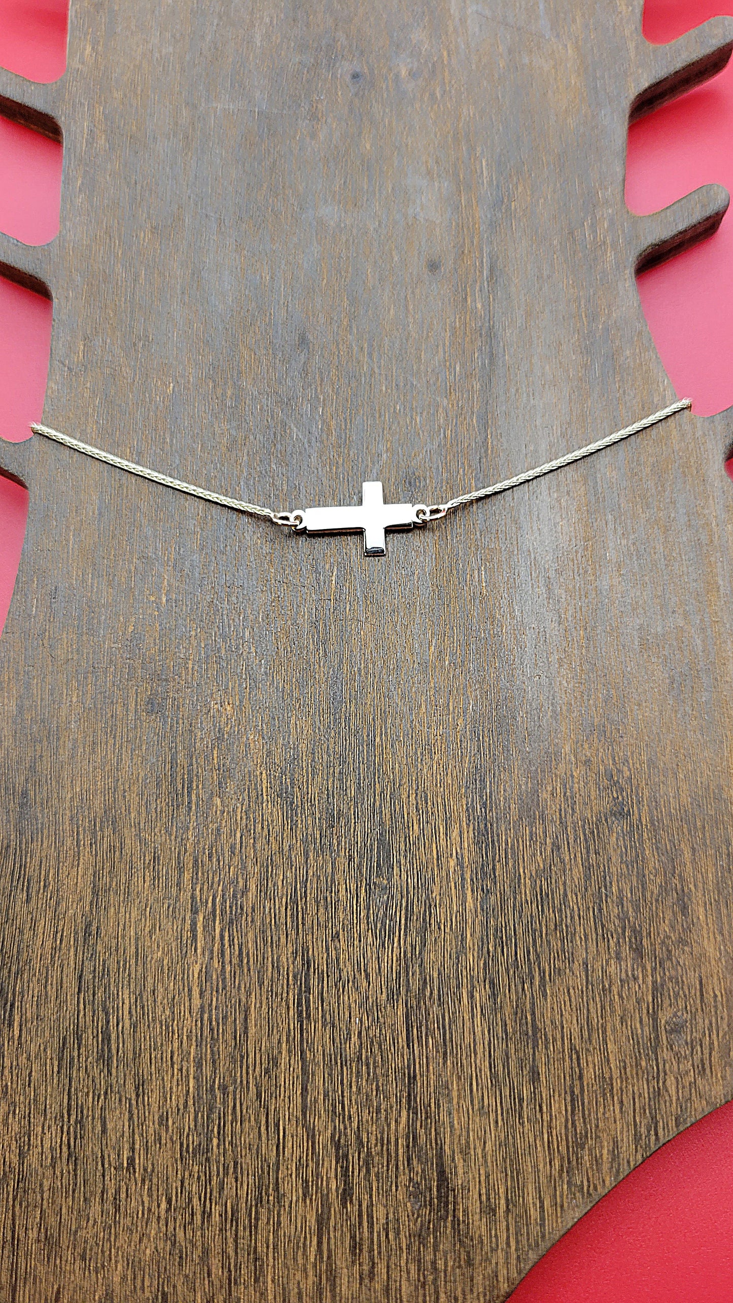 14k yellow gold Cross Anklet on a wooden foot display while on a red color background zoomed in.