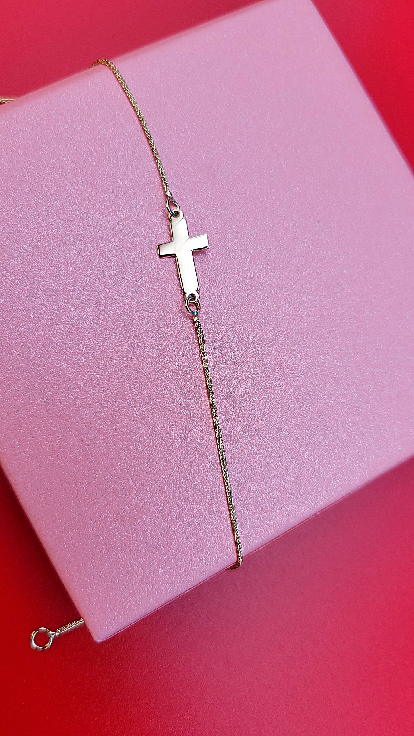 14k yellow gold Cross bracelet on a pink jewelry box zoomed out, red background.