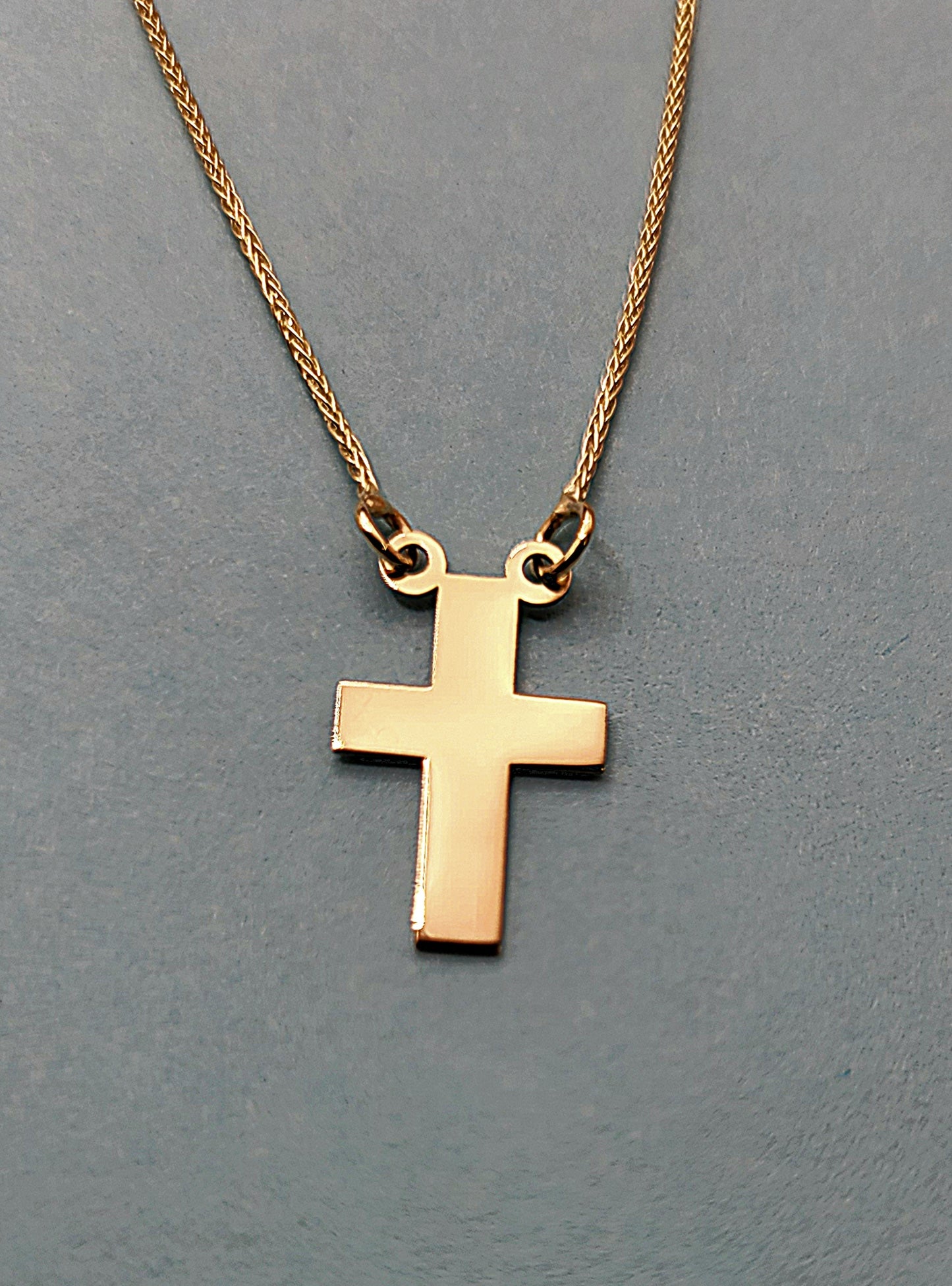 Our stunning 14k yellow gold Cross necklace displayed on a gray color background.