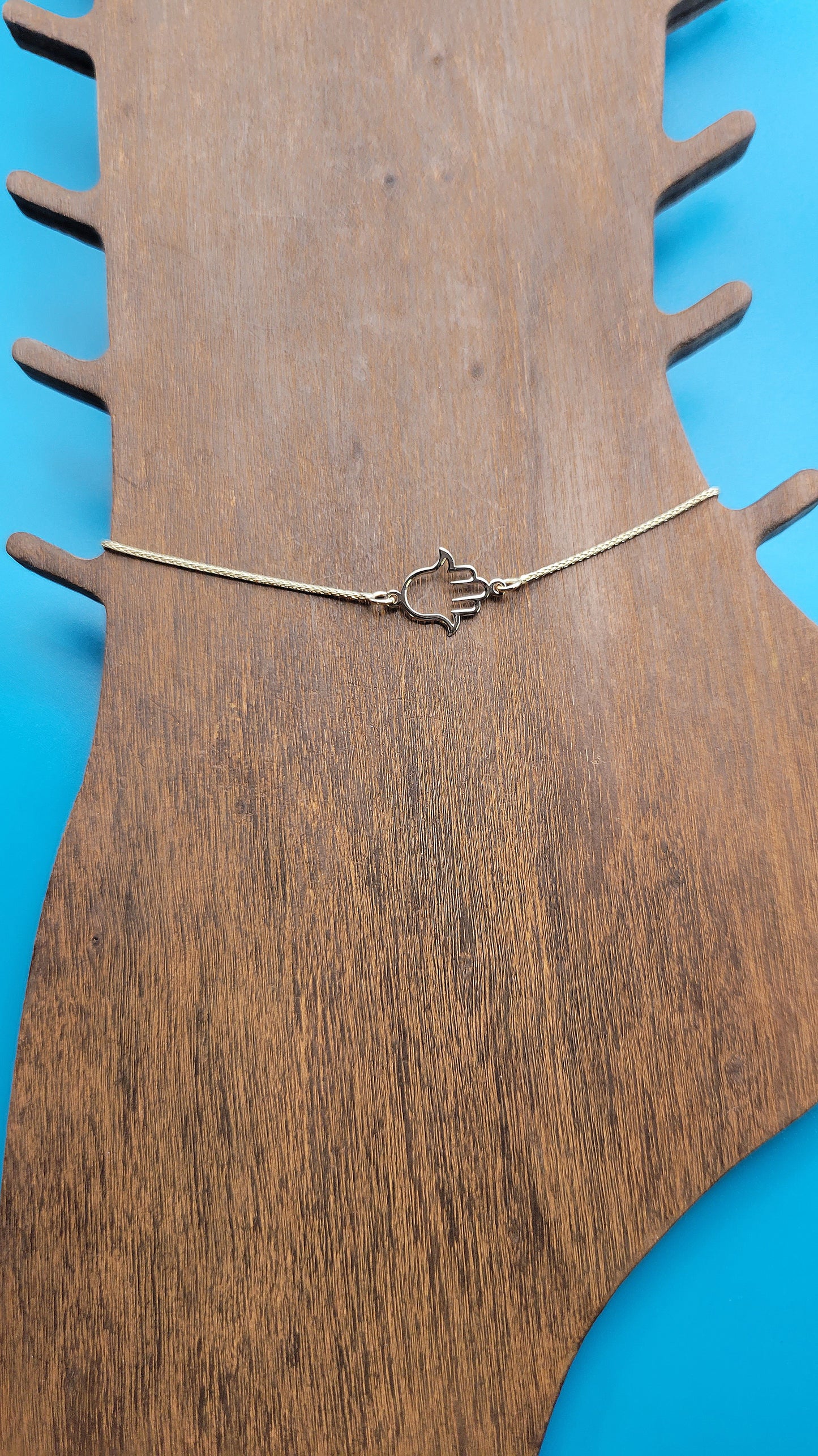 14k yellow gold Hamsa hand Anklet on a wooden foot display while on a blue color background zoomed