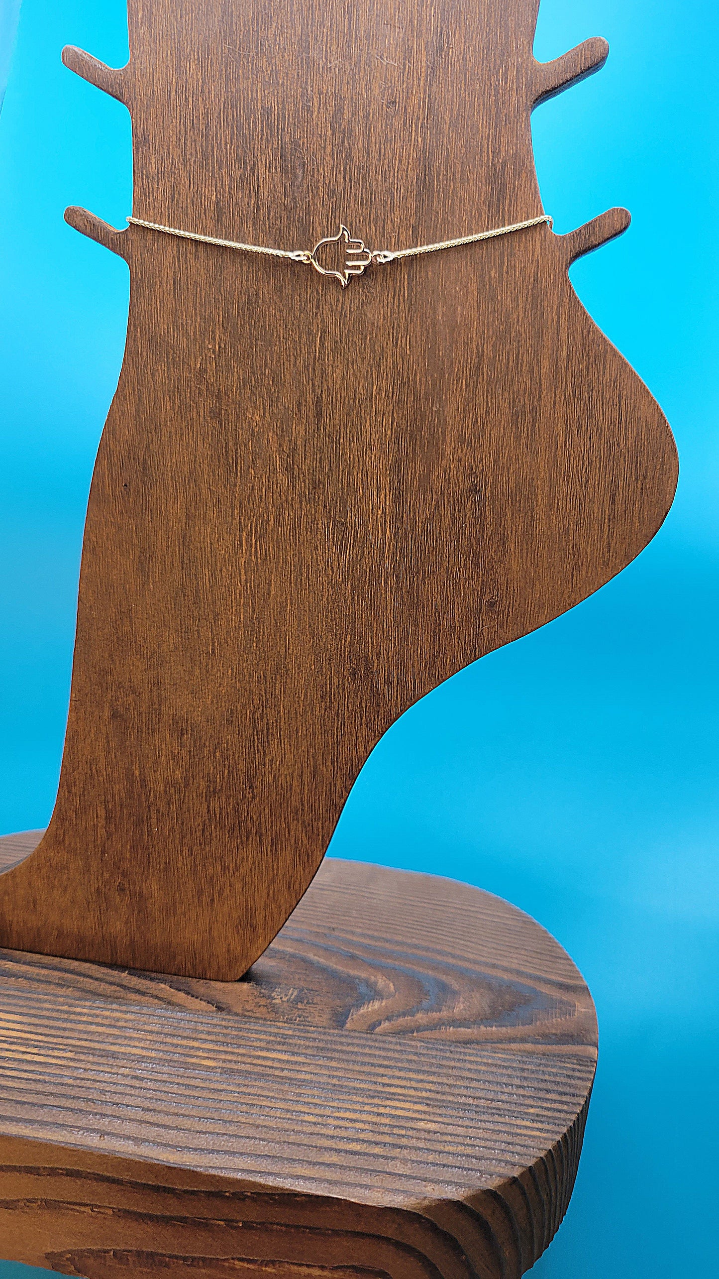 14k yellow gold Hamsa hand Anklet on a wooden foot display while on a blue color background.