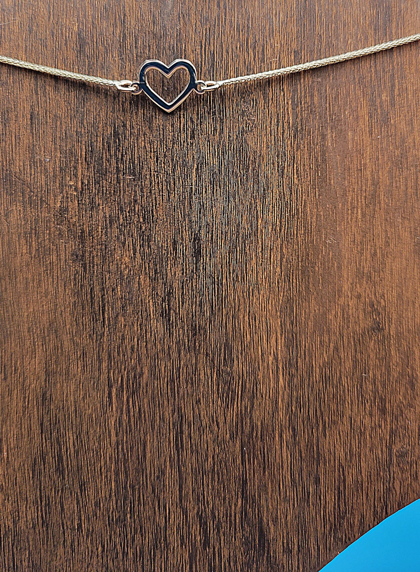 14k gold Hollow Heart Anklet on a wooden foot display on a blue color background zoomed in.