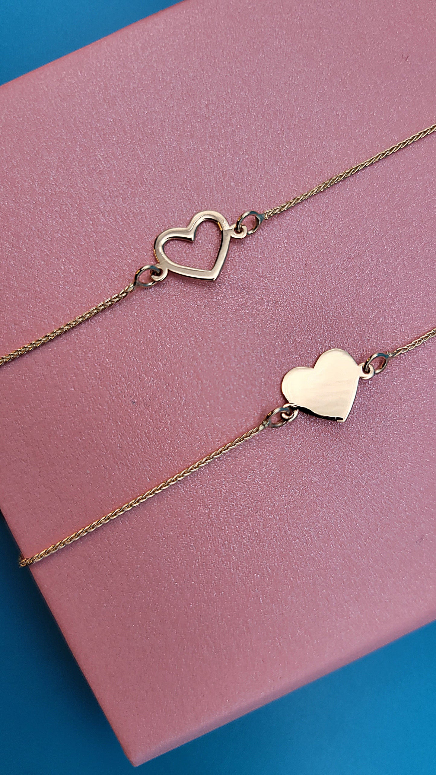 14k gold hollow and solid heart bracelets zoomed on a pink jewelry box zoomed, blue background.
