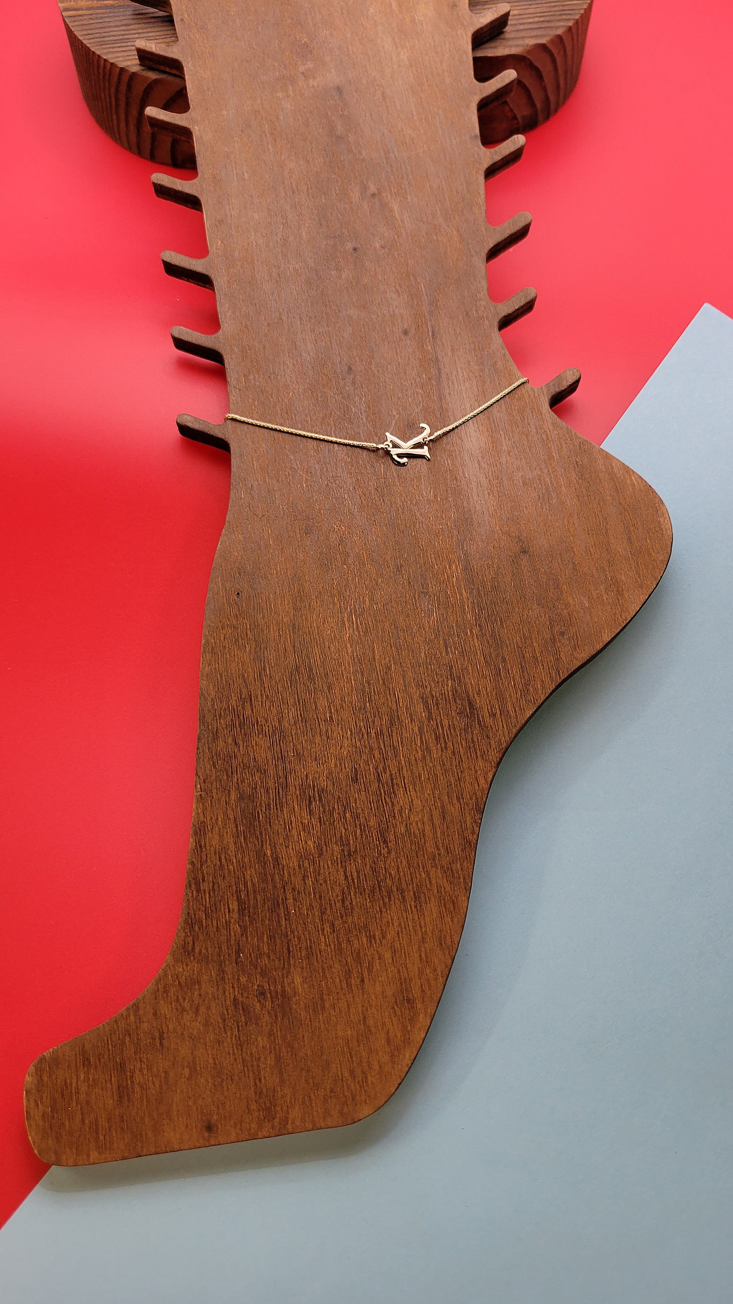 14k gold letter initial K Anklet on wooden foot display on a blue/red color background.