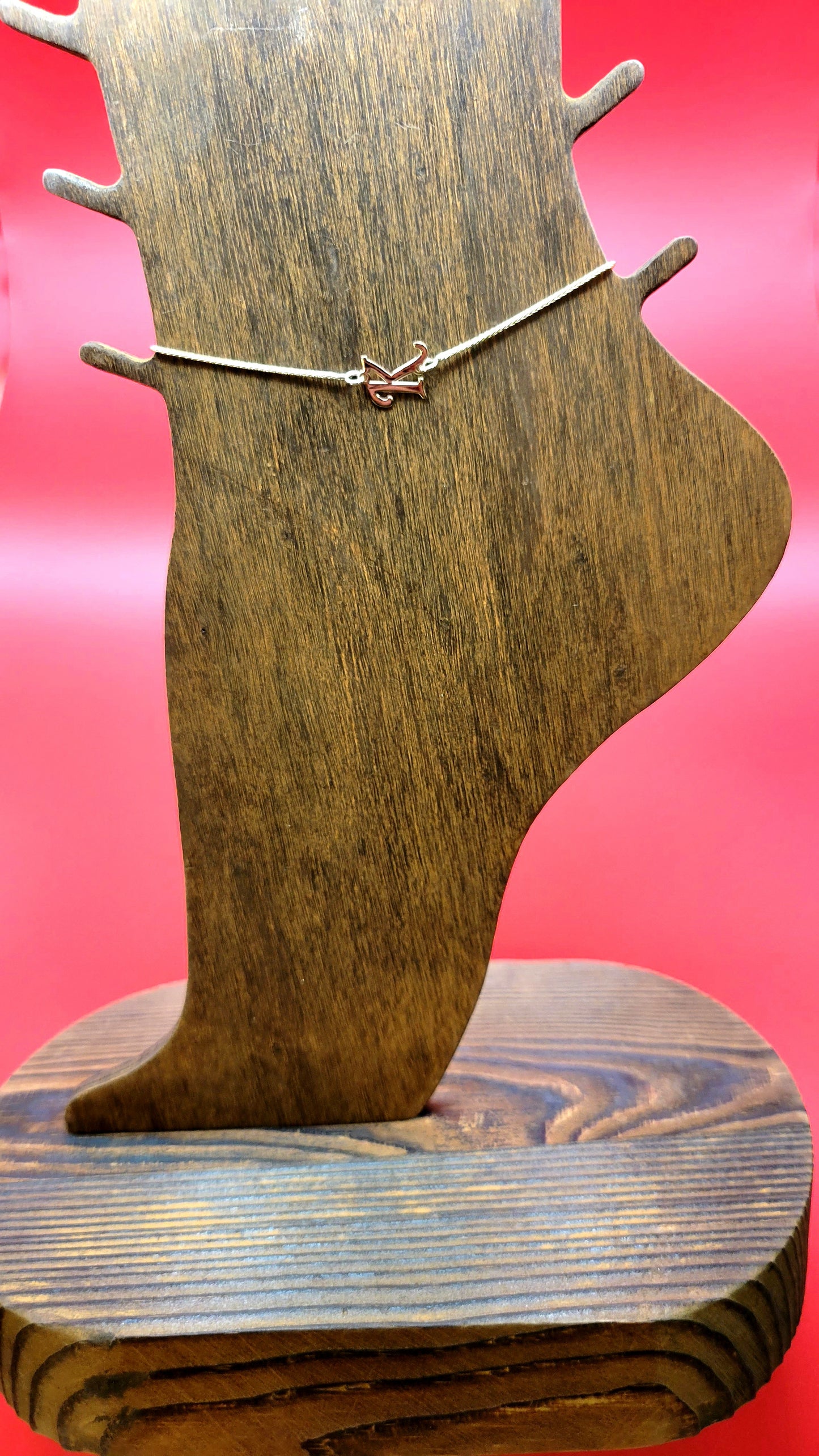 14k gold letter initial K Anklet on wooden foot display on a red color background close up.