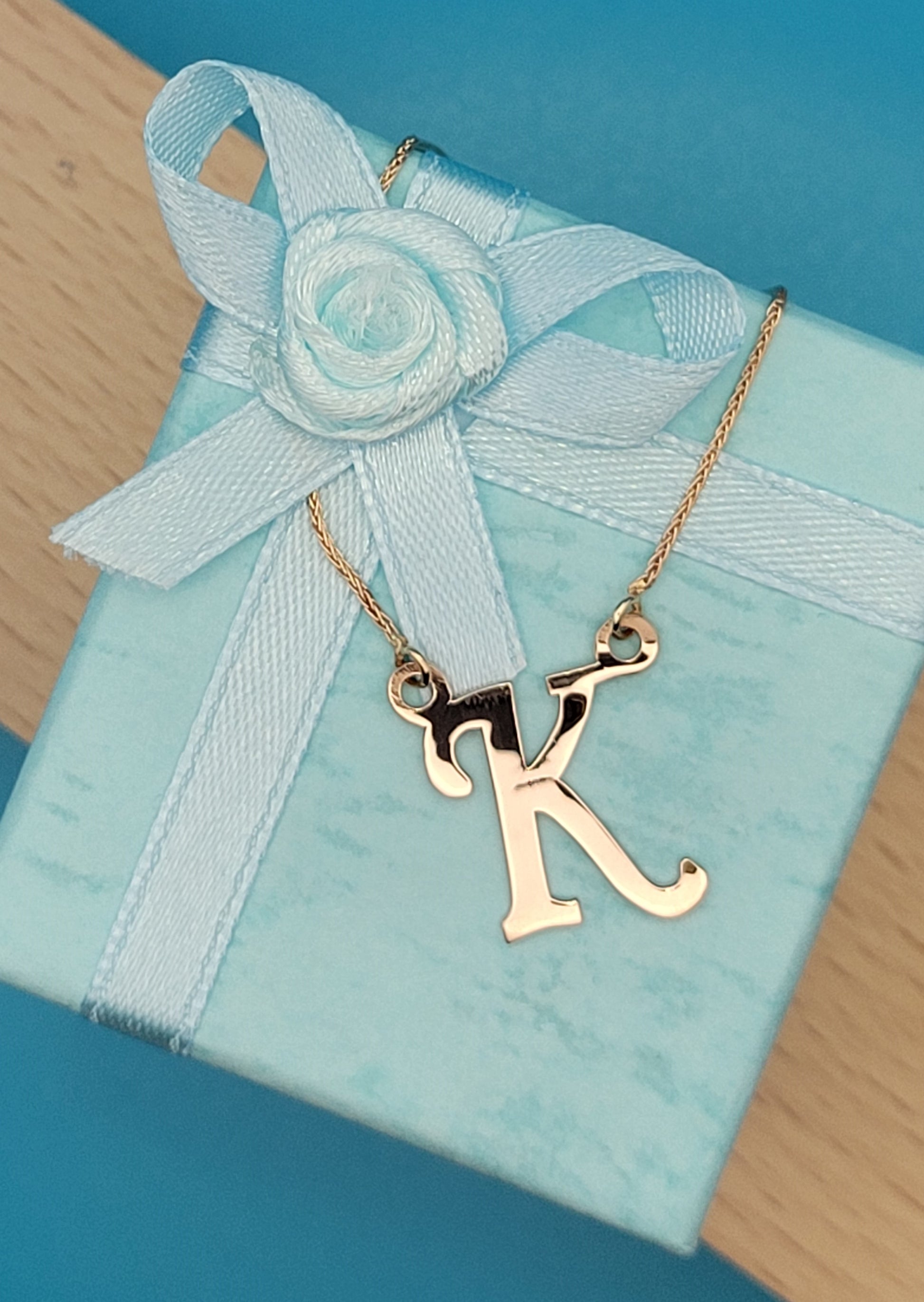 Rose gold 'K' necklace atop light blue jewelry box
