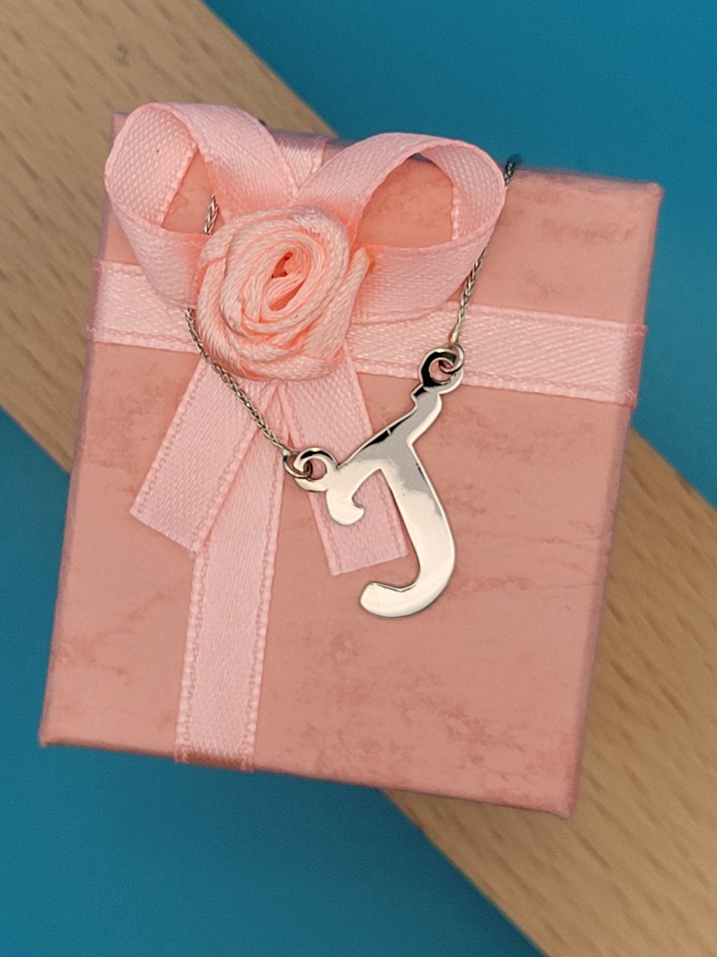 White gold 'J' necklace atop pink jewelry box