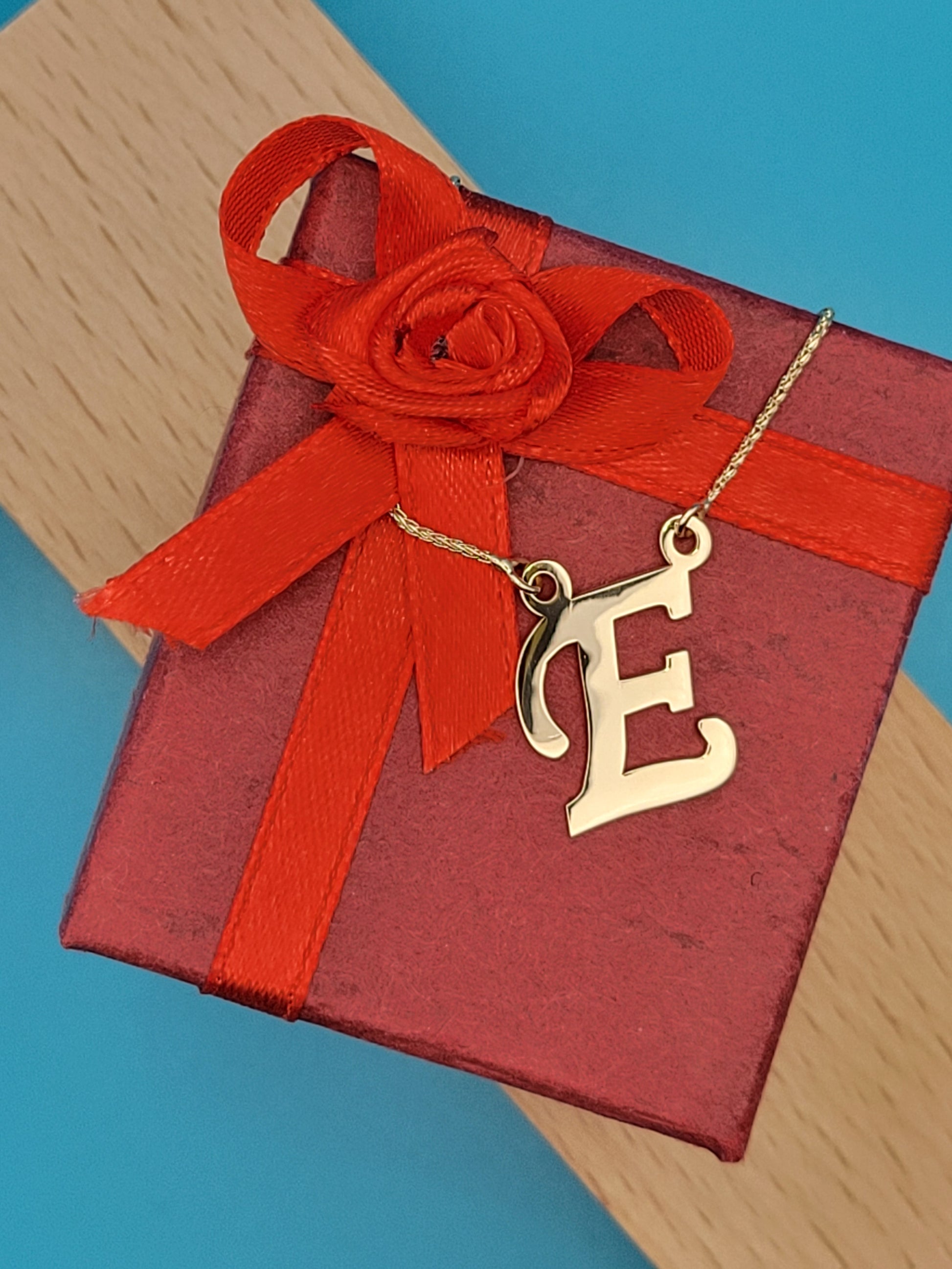Yellow gold 'E' necklace atop red jewelry box