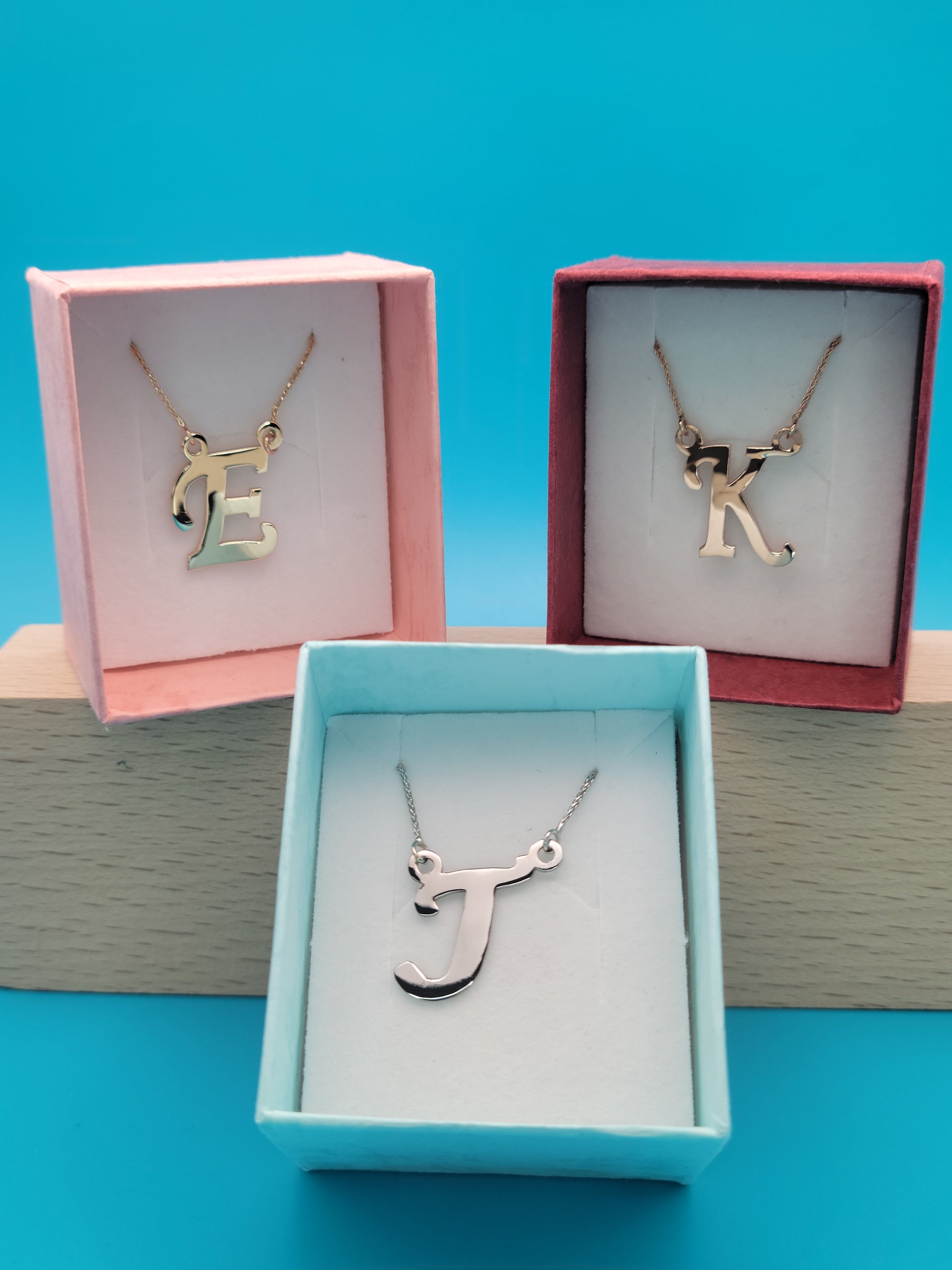 Colorful jewelry boxes: pink with gold 'E', blue with white gold 'J', red with rose gold 'K'